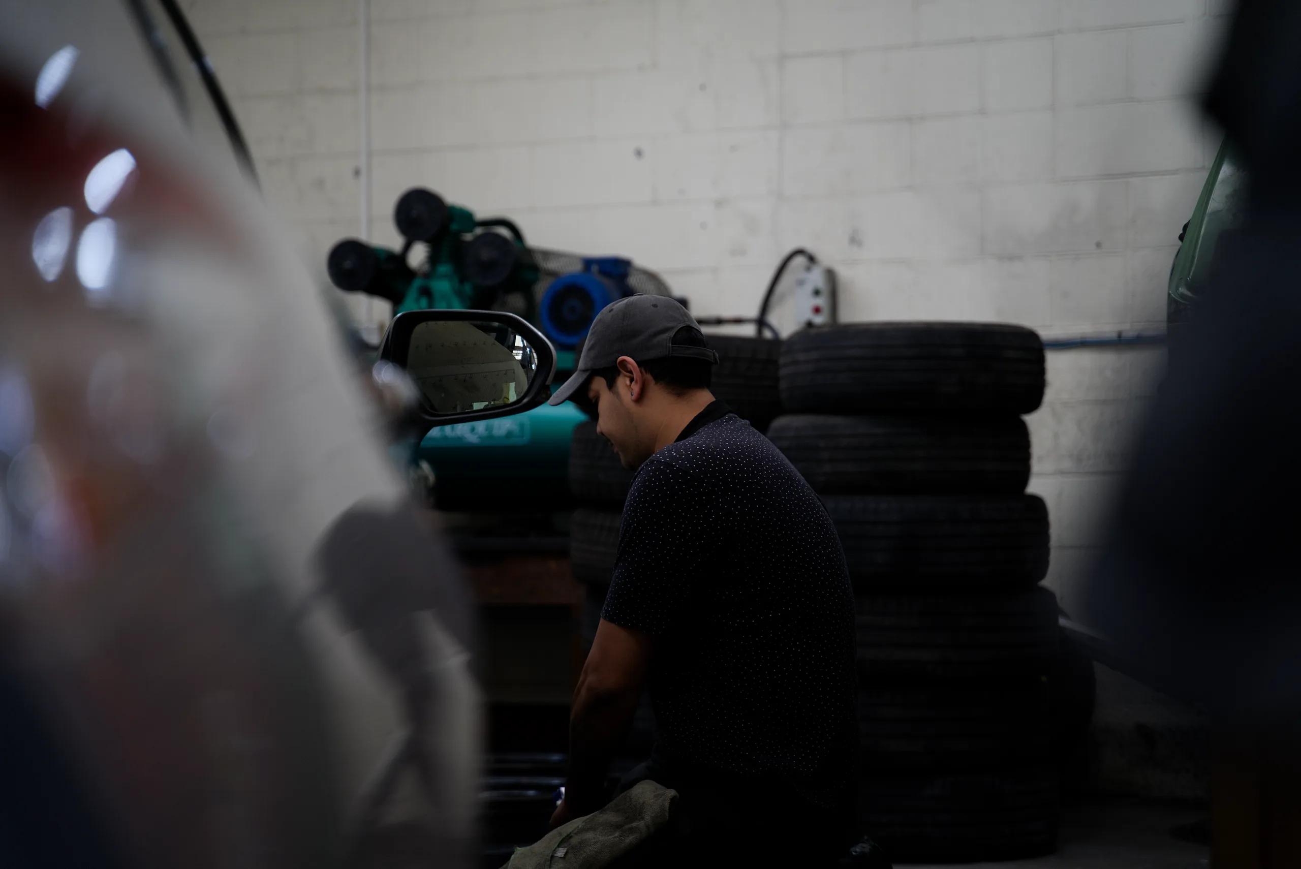 A mechanic at work beside a car, with stacked tyres behind